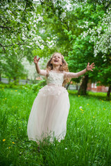 Obraz na płótnie Canvas Little beautiful girl in a smart white dress in blooming apple blossom garden.