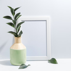 Mock up white frame and branch with green leaves in ligth-green vase on book shelf or desk. Minimalistic concept.