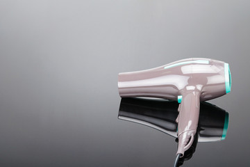 Brown hair dryer with green elements on the grey mirror background and copy space.