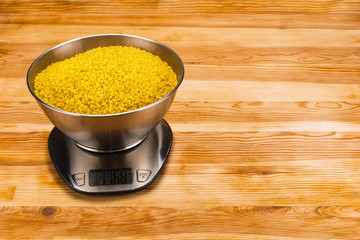 Bulgur in bowl on an electronic scale on a wood background with copy space