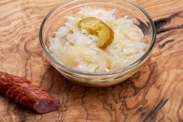 Traditional organic raw and fermented sauerkraut with pickled Persian cucumbers and grass fed beef smoked sausage stick on olive wood cutting board.