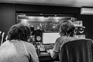 Music Engineer and Artist in Music Recording studio at mixing consol recording hip hop music viewing artists through glass