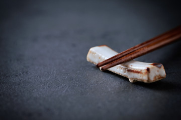 Wooden chopsticks and chopstick rest on black stone background. Close up. Copy space. 