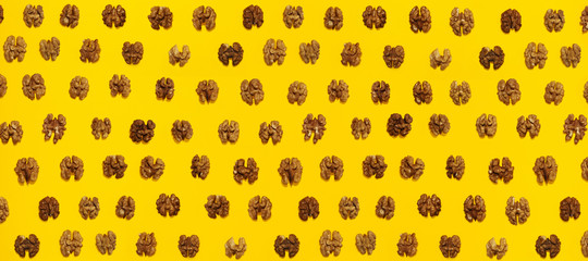 Walnuts halves in lines with hard shadow on yellow background, flat lay image.