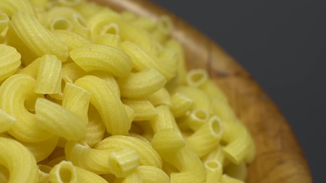 Raw macaroni in rotation. Elbow macaroni. Macaroni rigati close up.  Raw pasta  grey background. Italian cuisine concept.
