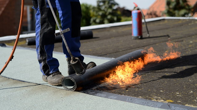 Handwerker Dienstleistung. Flachdach Haus Reparatur mit offener Flamme. Dachdecker verschwei&szlig;t drau&szlig;en Bitumen Dachabdichtung.