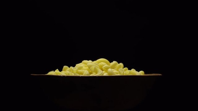 Raw macaroni in rotation. Elbow macaroni. Macaroni rigati close up.  Raw pasta  black background. Italian cuisine concept.