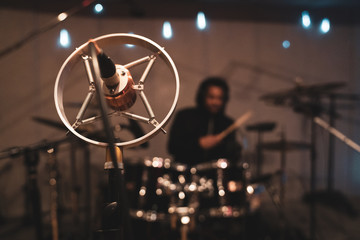 Music recording studio with microphone in foreground and African American drummer in background