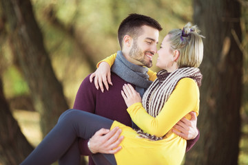 Young man carrying beautiful girlfriend in his arms in park