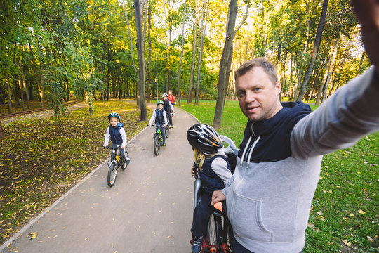 The theme family sports outdoor recreation. large family Caucasian 6 people mom dad and 4 children three brothers and sister ride bicycles in park on bicycle path. Father holds camera makes photo