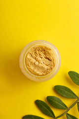  flat lay a jar eye shadow yellow summer color on a colored background with green leaves