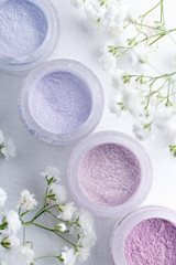Fototapeta na wymiar flat lay jars of eye shadow in pastel spring colors on a white textured background with delicate white flowers gypsophila