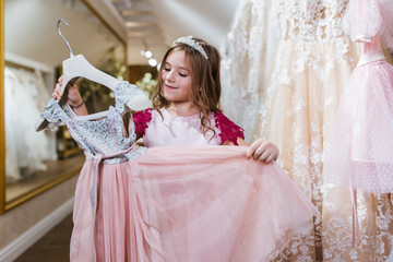 Charming little girl choosing new elegant dress for her.