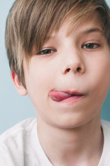 Confident calm boy shows his tongue and looks into camera