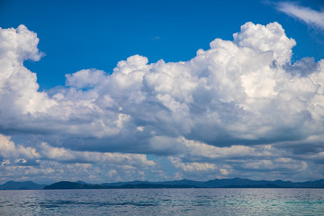 Naklejka na ściany i meble Blue sea and sky landscape with distant island. Romantic tropical cloudscape with green island photo background.
