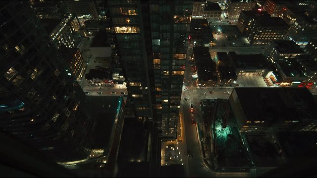Wide angle down shot of city skyscraper at night with lights on. Dark and moody with an epic feeling. Downtown big office buildings in a major city. Cars drive by with their lights on. 