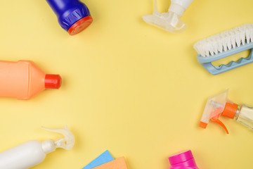 House cleaning supplies on  yellow background. Row of plastic bottles with cleaning liquid on wood, copy space on top.