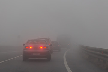 A group of cars with red lights on the road in the fog