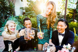 Happy multiethnic friends toasting drinks at table during cocktail party at sunset