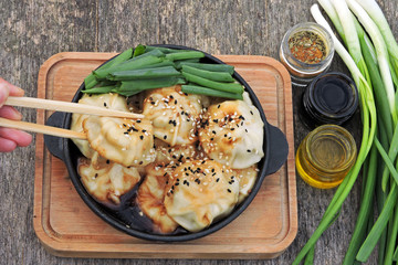 Chinese dumplings with green onions in a cast iron skillet on a wooden surface. Top view.