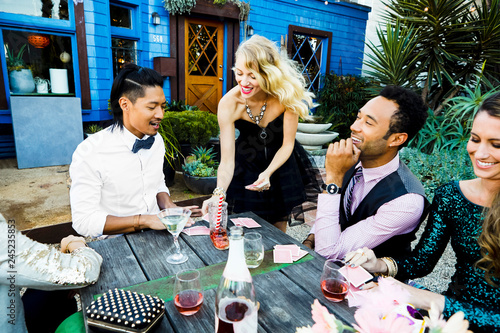 Smiling friends playing cards at table during cocktail party in backyard
