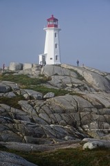 Fototapeta na wymiar Peggy’s Cove, Nova Scotia, Canada: Visitors tour the picturesque Peggy’s Point Lighthouse (1914) shrouded in morning mist.