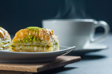 Traditional turkish dessert antep baklava with pistachio on white plate with cup of coffee or...