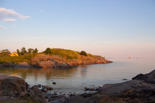The rocky shore of the island of Suomenlinna and the sea view in the Gulf of Finland at sunset on a summer evening in Finland.