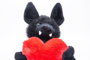 Stuffed funny black bat toy with red fluffy heart on white background