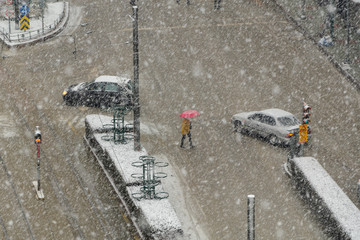 Snowfall in the city center.Woman is crossing the street in traffic