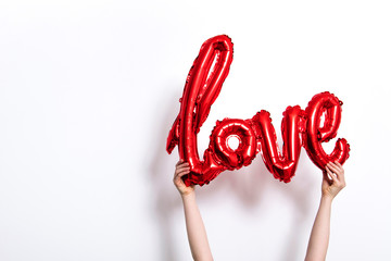 Red foil Love balloon held against a plain white background