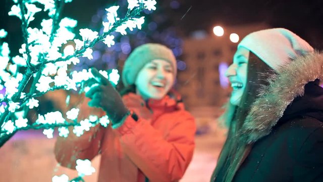 Two young girls walk in the winter through the decorated streets of the city. New year, holiday, snow