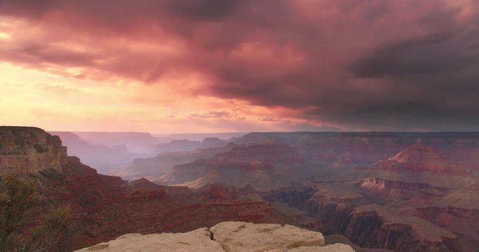 Dramatic shot of Grand Canyon at sunset with amazing lighting, clouds, red cliffs and blue skies in 4K DCI. Camera pans right.
