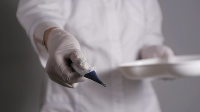 Female doctor giving medication. Young medical professional gives digital thermometer taking from kidney dish.