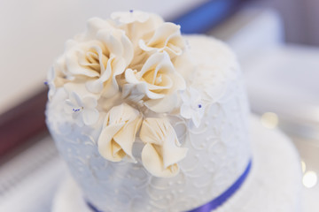 Wedding cake with ice and blue ribbon decoration and white roses on the top tier