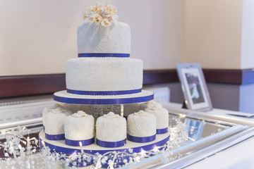Wedding cake with ice and blue ribbon decoration and white roses on the top tier