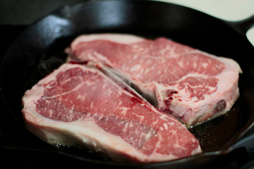 New York strip steaks cooking in a cast iron pan on a natural gas stove top.
