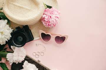 Obraz na płótnie Canvas Stylish feminine flat lay with pink peonies, hat,photo camera, retro sunglasses, jewelry,purse and nail polish on pastel pink paper with copy space. International Women's Day. Hello spring