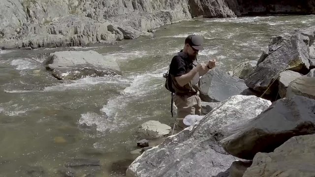 Fly fisherman ties a fly on in a fast moving river in Colorado