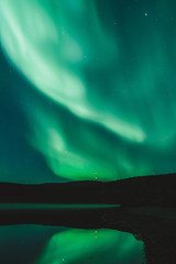 Green Northern Lights and stars in the night sky over the lake. Observing Aurora Borealis at North. Light phenomenon in the Arctic Circle. Abstract background with copy space. 