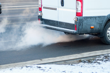 Pollution of the atmosphere by gas from the exhaust pipe of a white van in motion in the city....