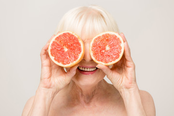Senior woman beauty concept biting grapefruit, studio portrait isolated on white background.