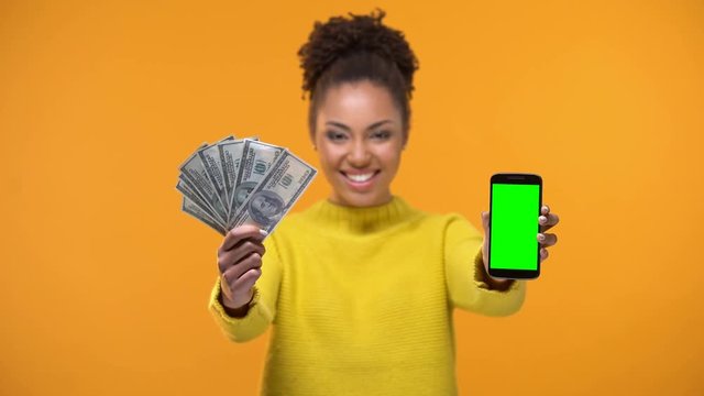 African-American woman showing smartphone and bunch of dollars, money transfer