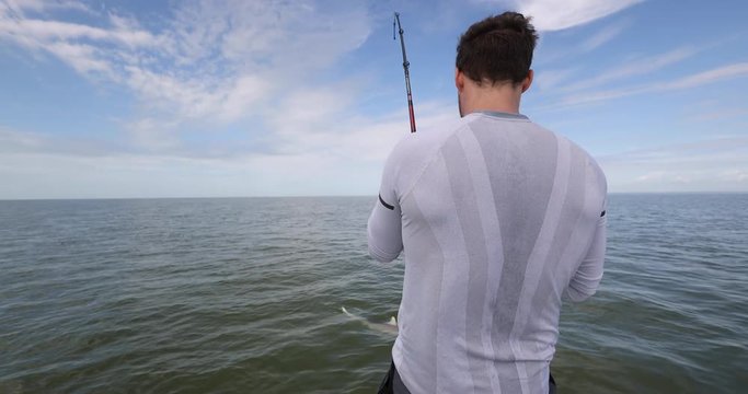 Sport fishing - man shark fishing on boat in Florida with shark hooked. Man fishing with hook and line catching a shark and fighting hard reeling it in catch and release of spinner shark, Florida keys