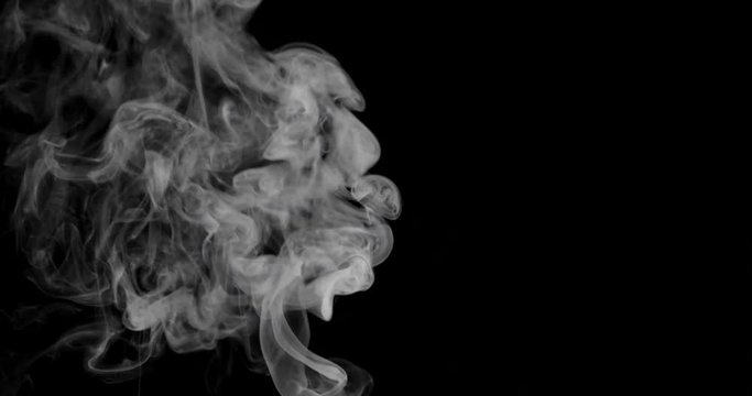 White cloud of smoke or vapor rises against a black background in slow motion.