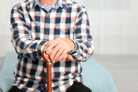Elderly man with walking cane sitting on bed, closeup. Space for text