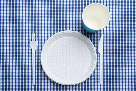 Table setting with plastic dishware on plaid fabric, flat lay