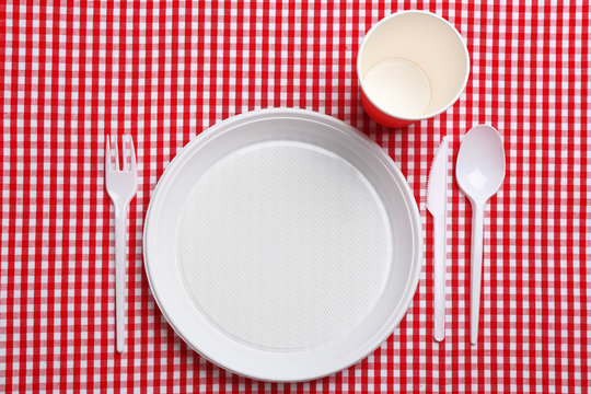 Table setting with plastic dishware on plaid fabric, flat lay