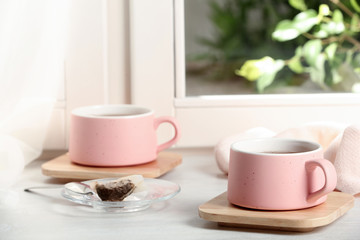 Cups of hot tea with wooden coasters on window sill
