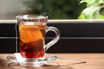 Glass cup of hot tea on wooden window sill. Space for text